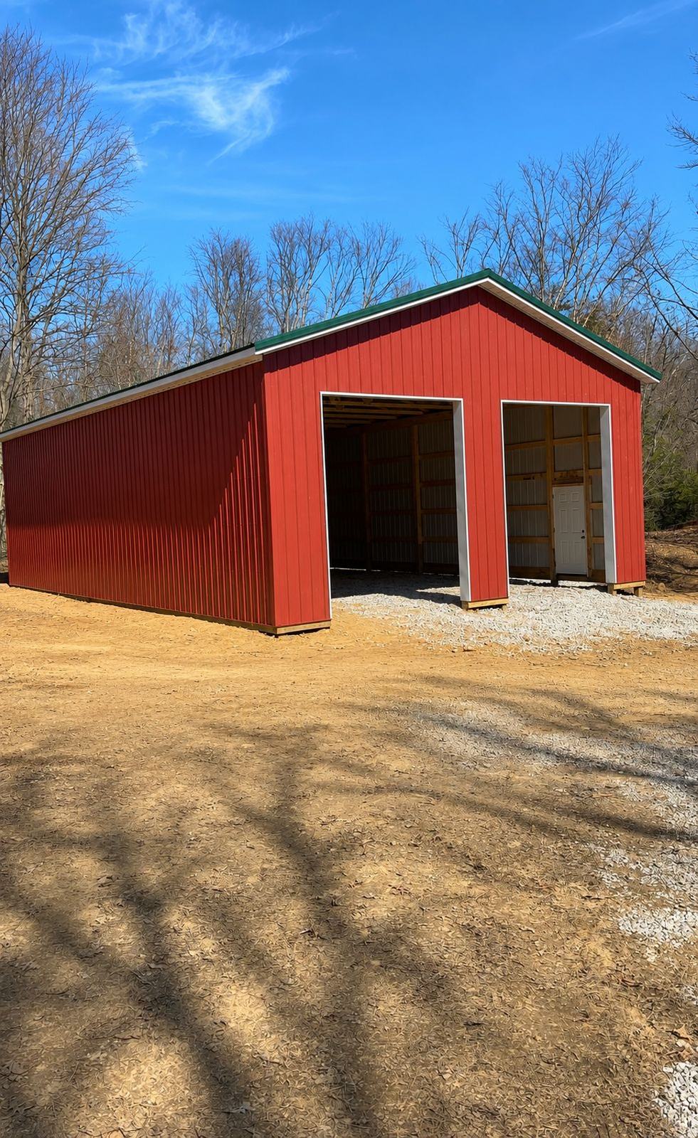 Red pole barn with a green roof and an open bay